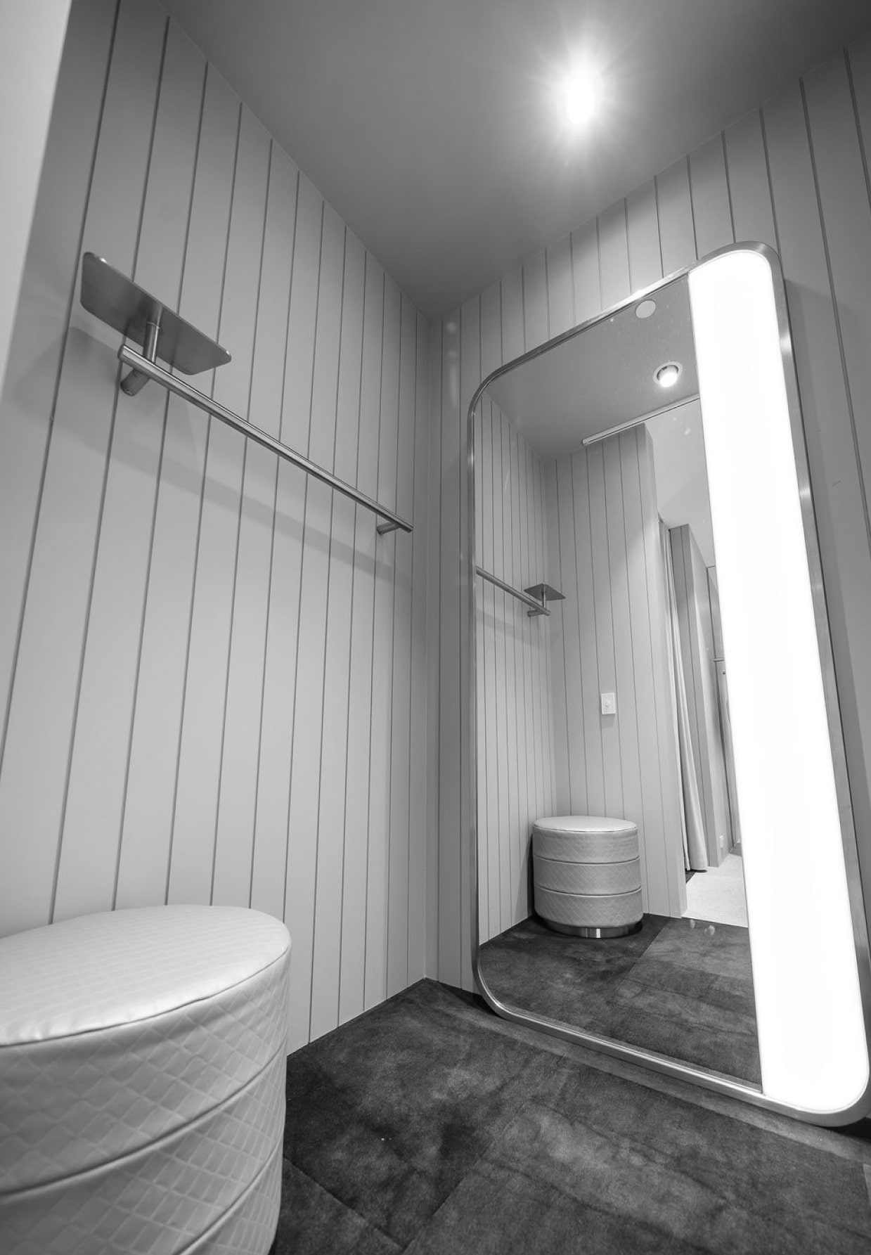 Dressing room with full-length mirror and ottoman, vertical wood paneling, modern lighting enhances elegant interior space.