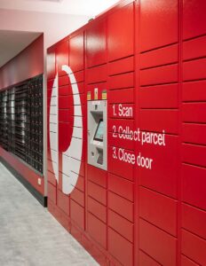 Red parcel locker with scan instructions and touchscreen for package collection in postal service hallway.