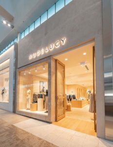"Modern clothing store facade with glass display, showcasing fashion apparel and accessories inside a well-lit interior."