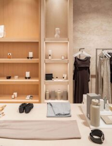 Elegant retail boutique interior with minimalistic shelving, clothing, accessories, skincare products, and stylish decor.