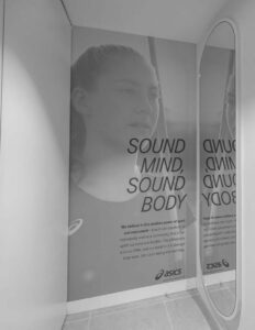 "Asics ad with woman, mirror reflection, slogan 'Sound Mind, Sound Body,' promoting positive power of sport and movement."