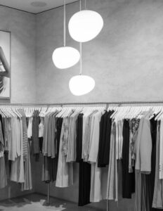 Modern clothing store interior with hanging lights, displaying neatly arranged garments on hangers.