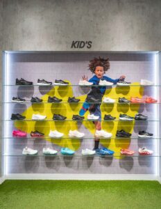 Kids' athletic shoe display with colorful sneakers on glass shelves in a vibrant retail setting.