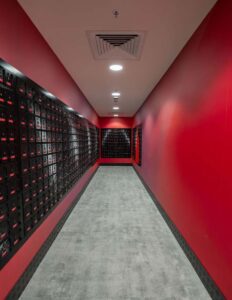 Red hallway with numerous black electrical panels lining the walls, ceiling with ventilation system and lights.