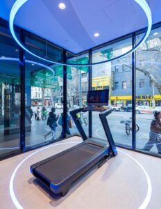 Modern treadmill in futuristic gym with glass walls, blue lighting, street view in background.