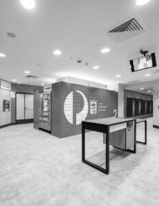 Modern post office interior with parcel lockers, a vending machine, and a service counter in monochrome setting.