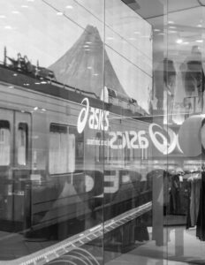 Storefront glass reflecting train, mountain, and ASICS branding in black and white.