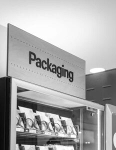 Modern vending machine with packaging supplies, labeled "Packaging," in a black and white retail setting.